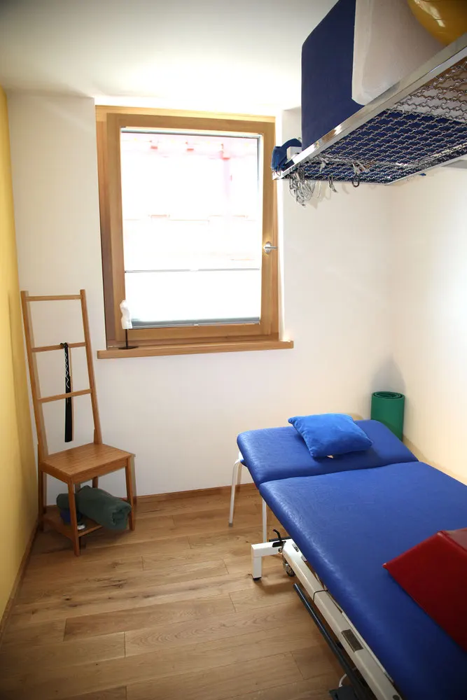 Kleiner Behandlungsraum mit Liege und Holzfenster
